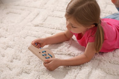 Photo of Cute little girl playing with wooden lacing toy on carpet indoors, space for text