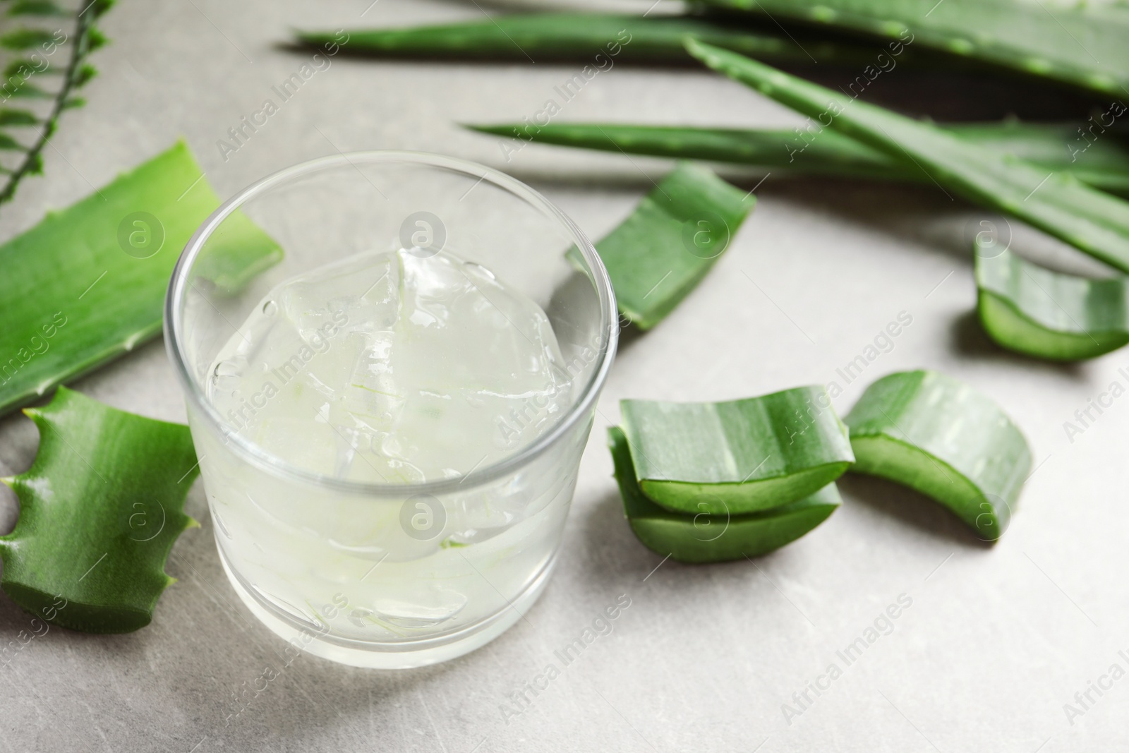 Photo of Glass with peeled aloe vera and green leaves on gray table