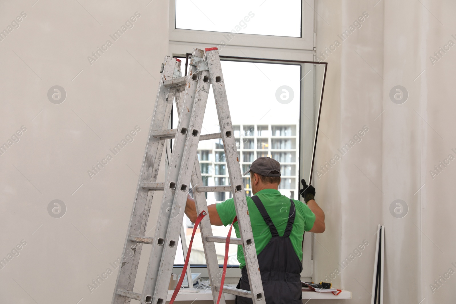 Photo of Worker in uniform installing double glazing window indoors, back view