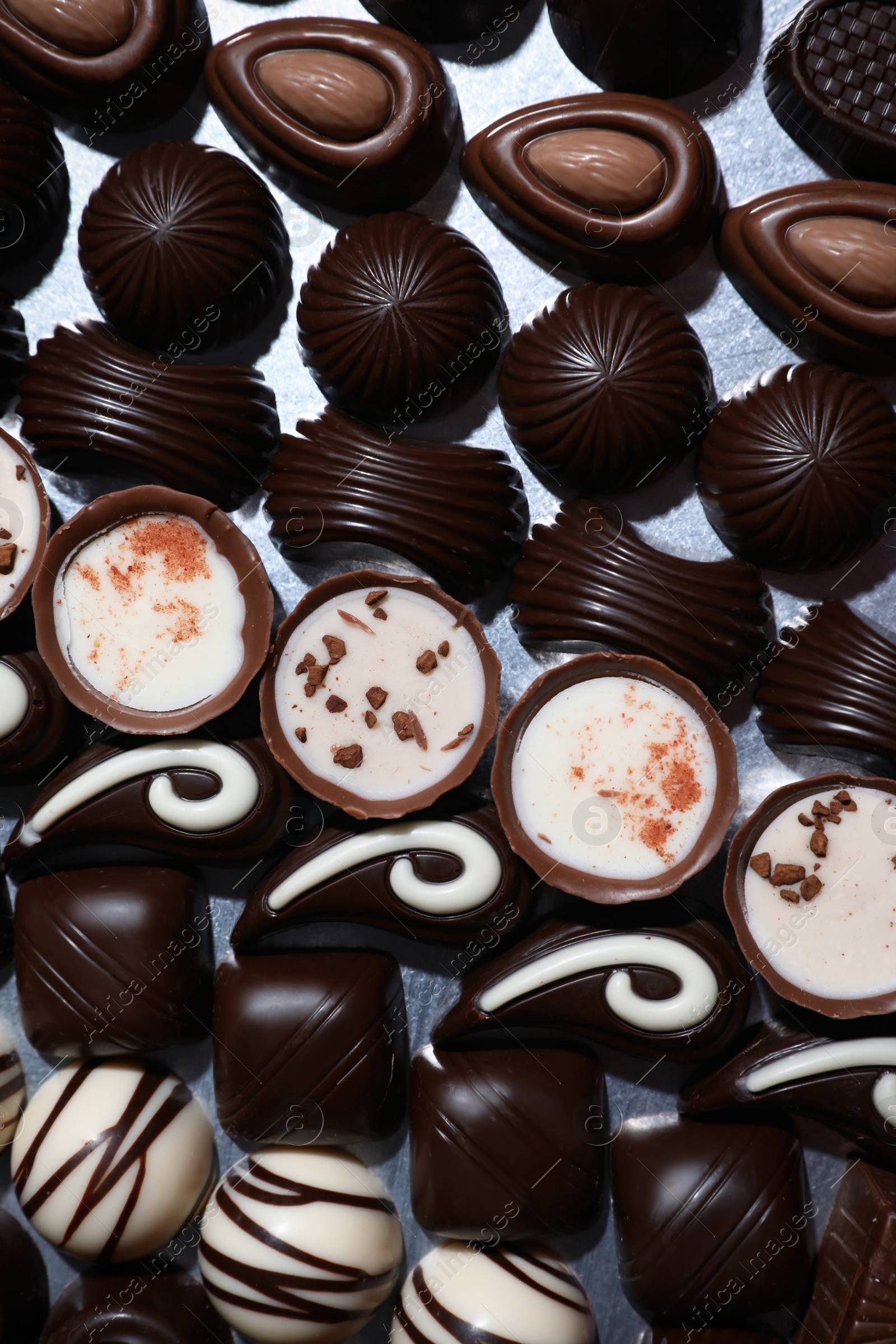 Photo of Many different delicious chocolate candies on metal surface, top view