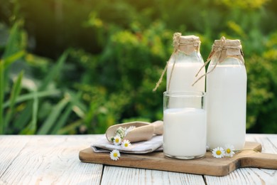 Tasty fresh milk and chamomile flowers on white wooden table outdoors, space for text