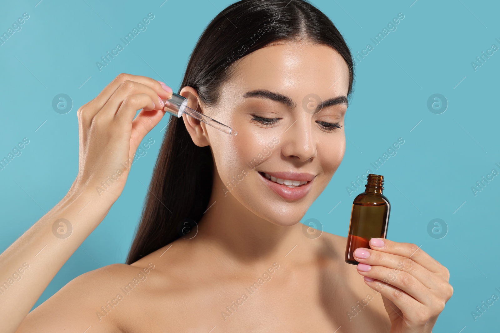 Photo of Beautiful young woman applying serum onto her face on light blue background