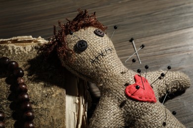 Voodoo doll with pins, old book and beads on wooden table, closeup