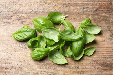 Photo of Fresh basil leaves on wooden table, above view