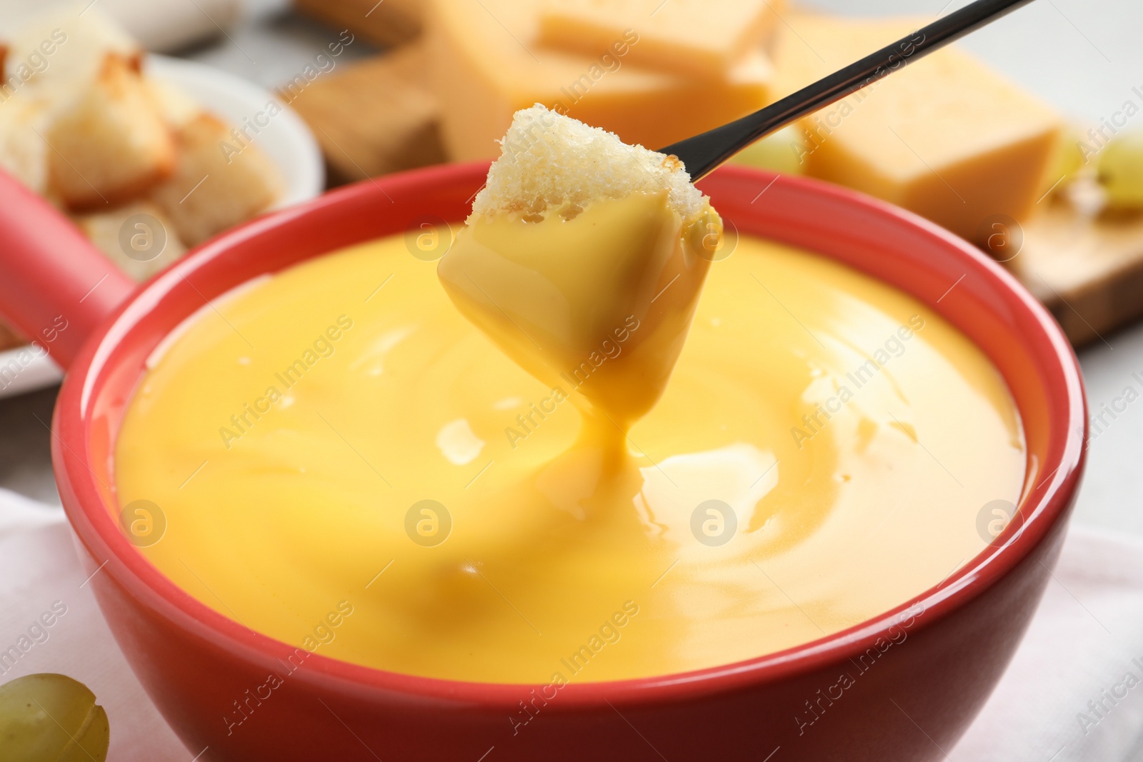 Photo of Dipping piece of bread into tasty cheese fondue, closeup