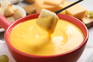 Dipping piece of bread into tasty cheese fondue, closeup