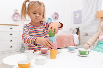 Photo of Cute little girl playing tea party at table in bedroom