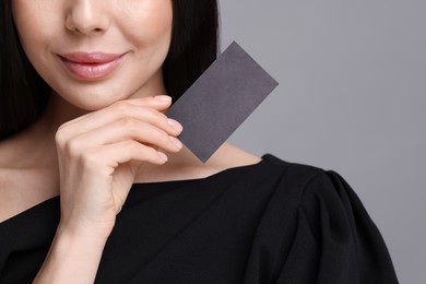 Woman holding blank business card on grey background, closeup. Space for text