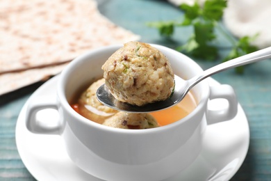 Photo of Spoon with matzoh ball over bowl of soup on table, closeup. Jewish cuisine