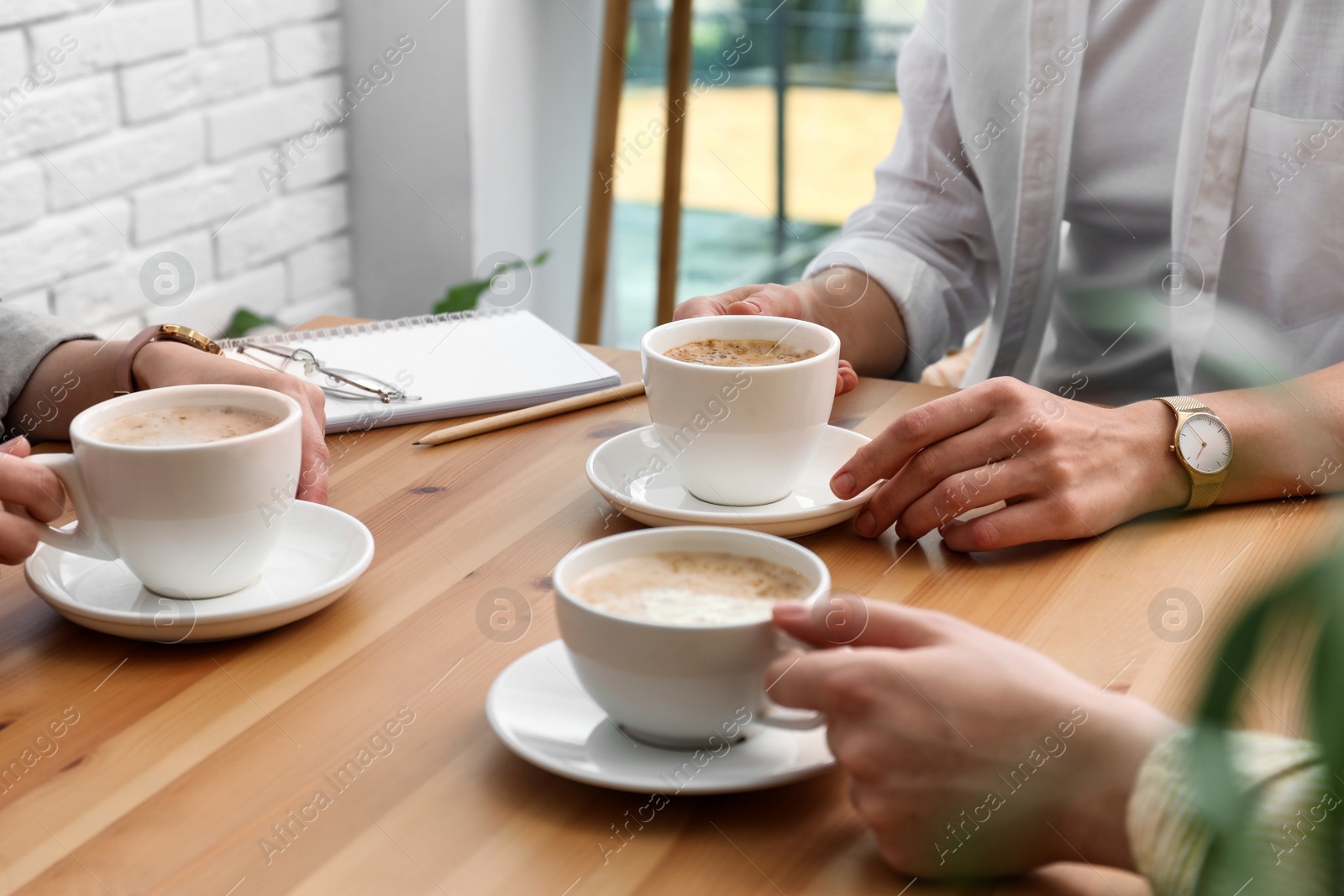 Photo of Women with cups of coffee at table in cafe, closeup