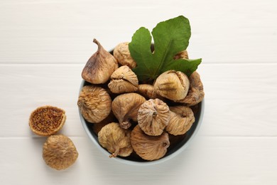 Bowl with tasty dried figs and green leaf on white wooden table, top view