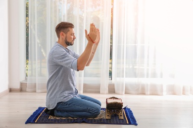 Photo of Muslim man with Koran praying on rug indoors