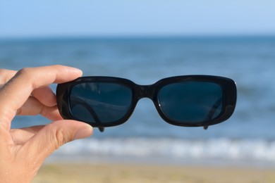 Photo of Woman holding stylish sunglasses near beautiful sea, closeup