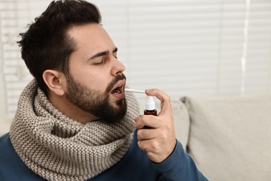 Photo of Young man with scarf using throat spray indoors