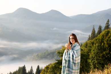 Photo of Woman with cozy plaid enjoying cup of hot beverage in mountains