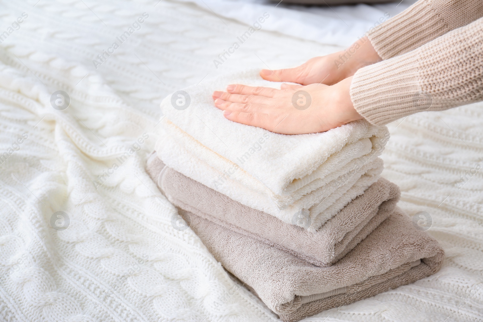 Photo of Woman folding clean towels on bed, closeup