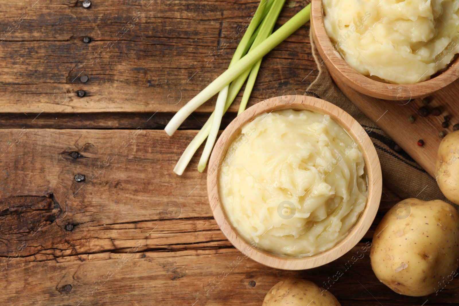 Photo of Bowls of tasty mashed potato, pepper and leeks on wooden table, flat lay. Space for text
