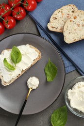 Photo of Pieces of bread with cream cheese, basil leaves and tomatoes on gray table, flat lay