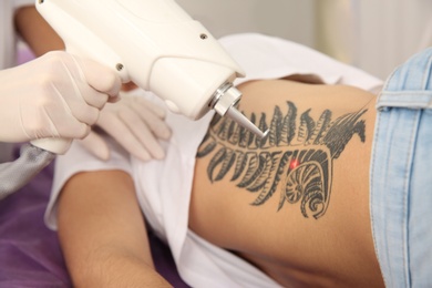 Photo of Young woman undergoing laser tattoo removal procedure in salon, closeup