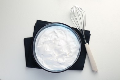 Bowl with whipped cream and whisk on light background, top view