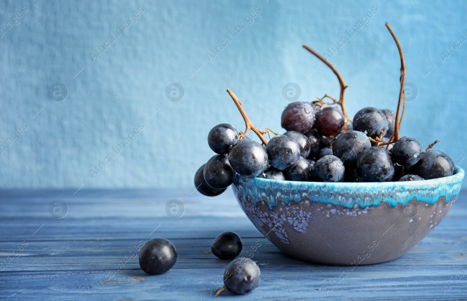Photo of Fresh ripe juicy grapes in bowl on table against color background with space for text