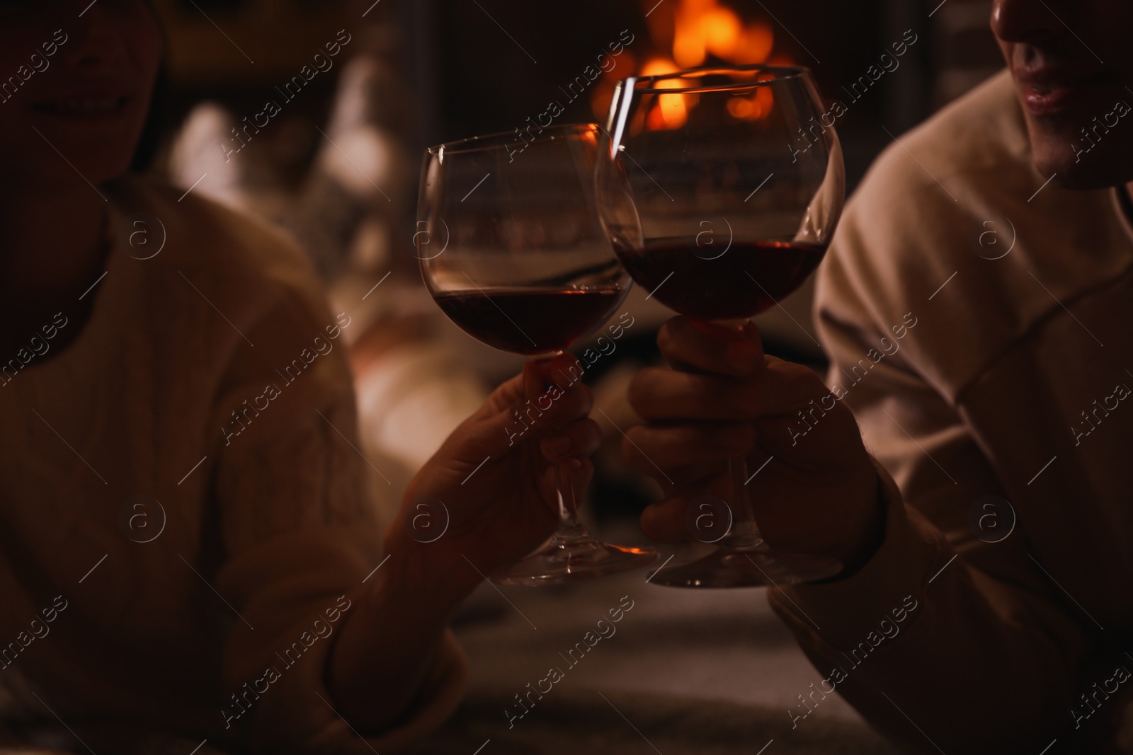 Photo of Couple with glasses of red wine near burning fireplace, closeup