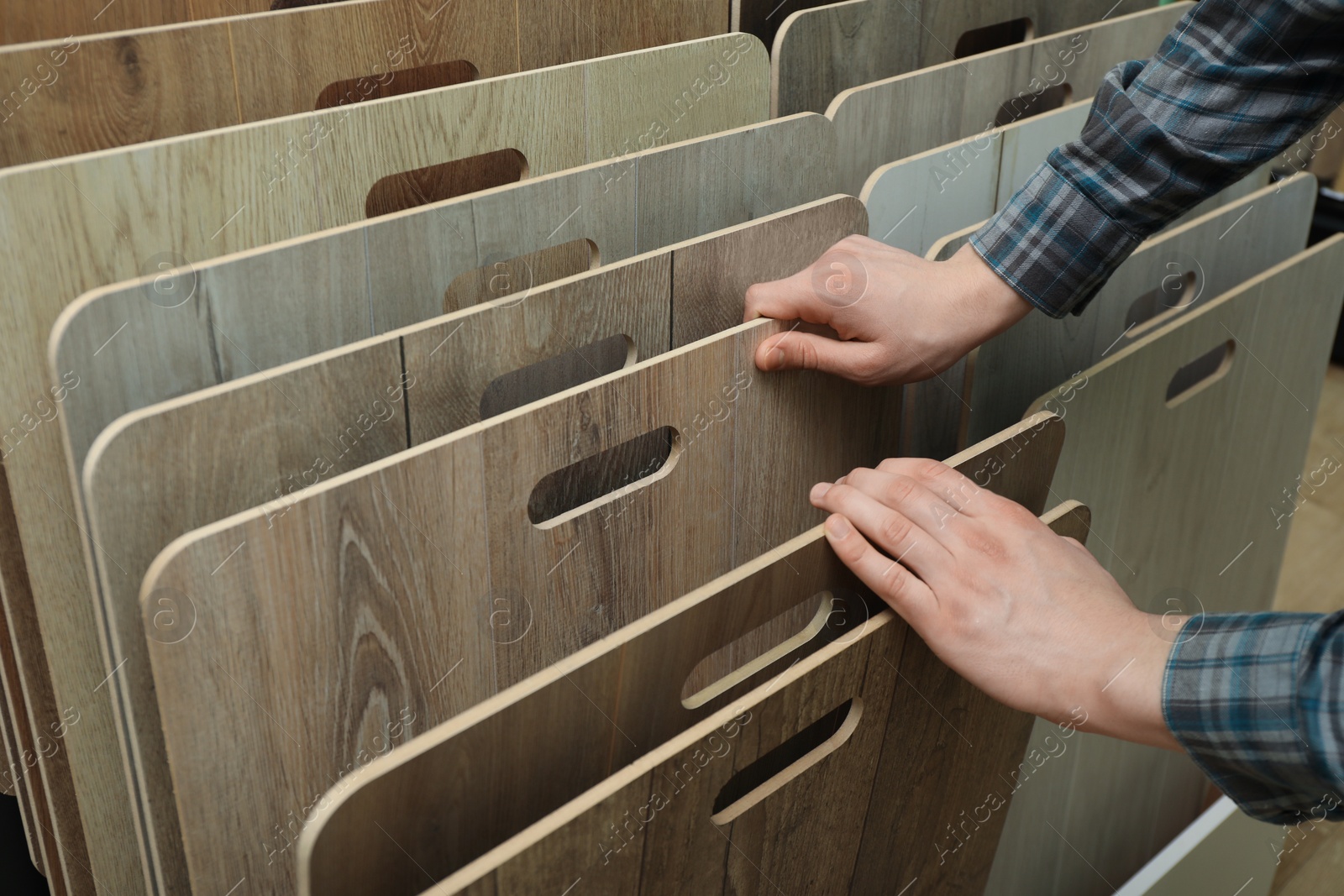 Photo of Man choosing wooden flooring among different samples in shop, closeup