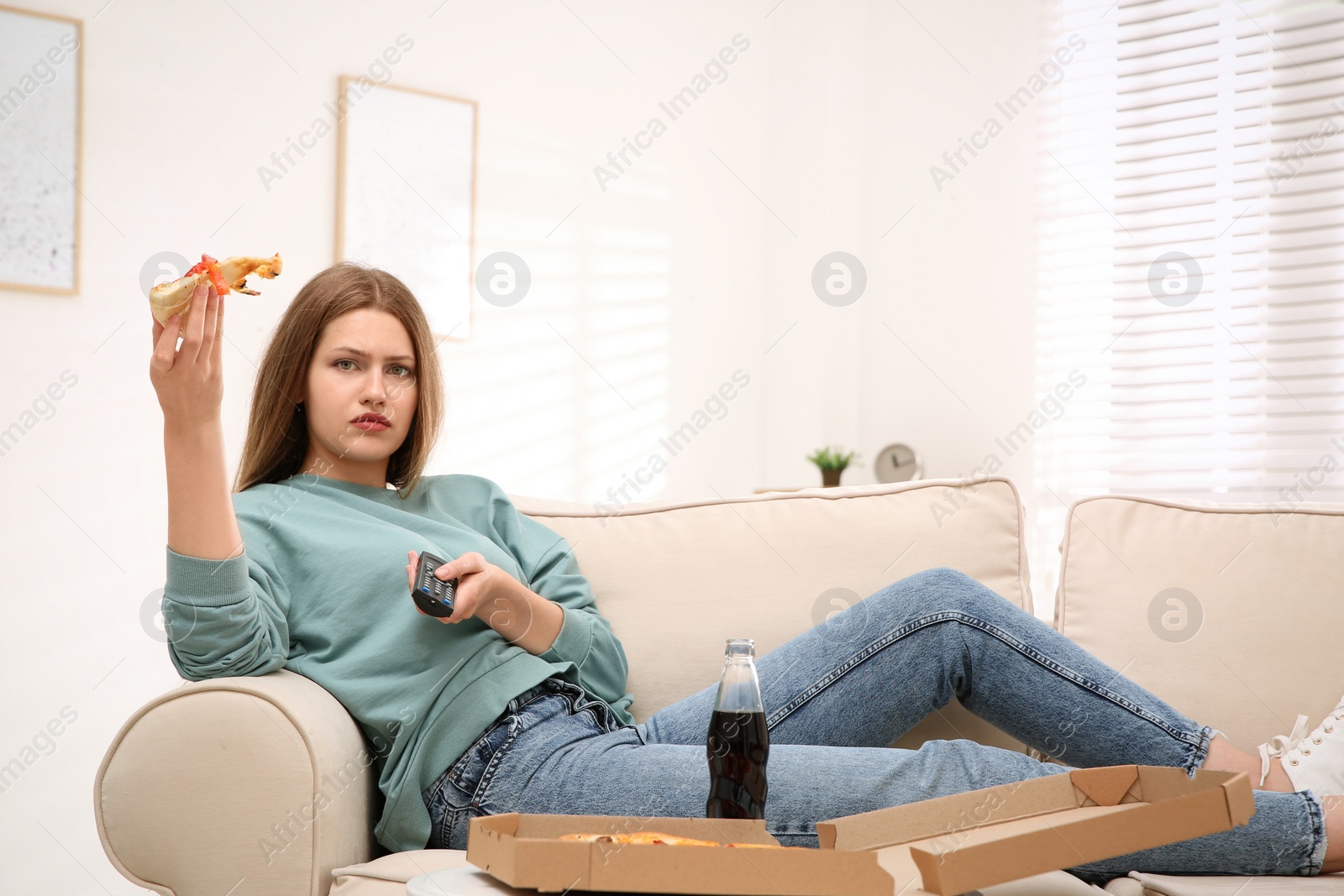 Photo of Lazy young woman with pizza and drink watching TV at home