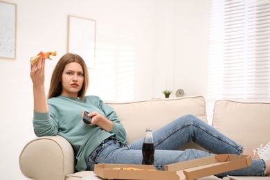 Photo of Lazy young woman with pizza and drink watching TV at home