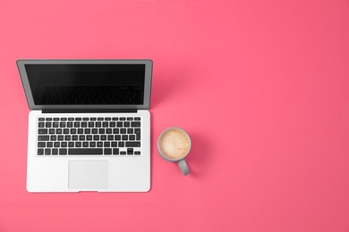 Photo of Modern laptop and cup of coffee on pink background, top view. Space for text