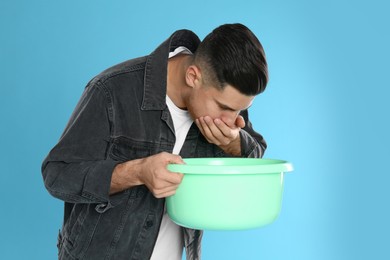 Man with basin suffering from nausea on light blue background. Food poisoning