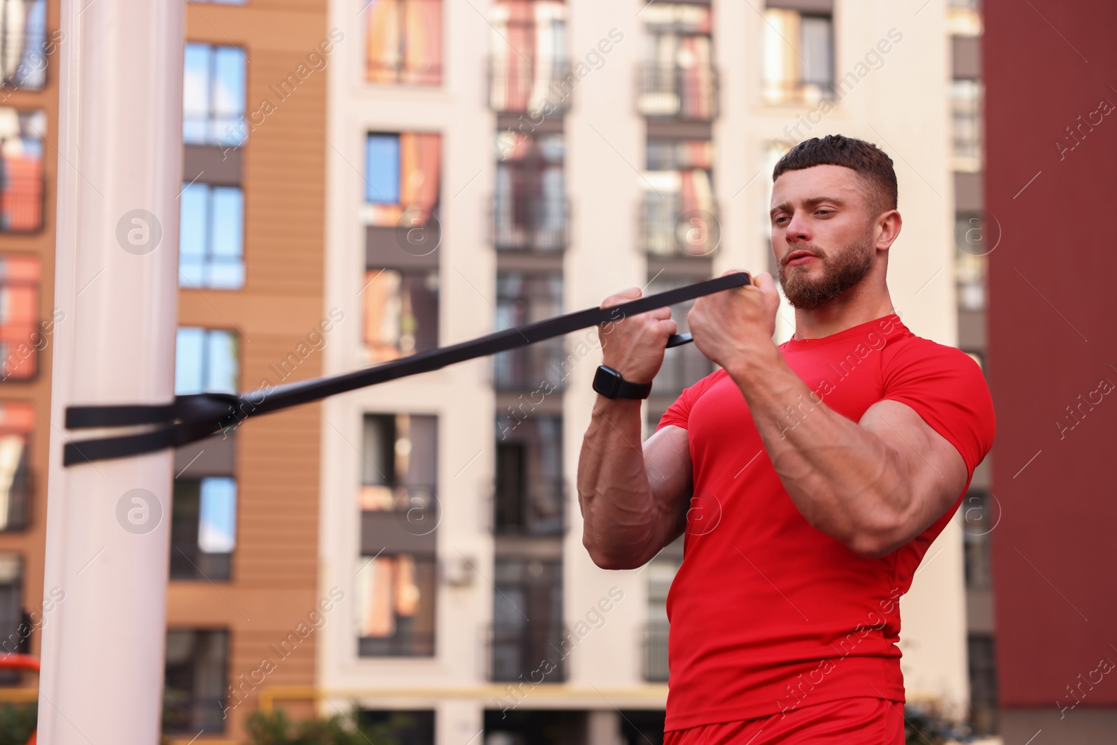 Photo of Muscular man doing exercise with elastic resistance band on sports ground