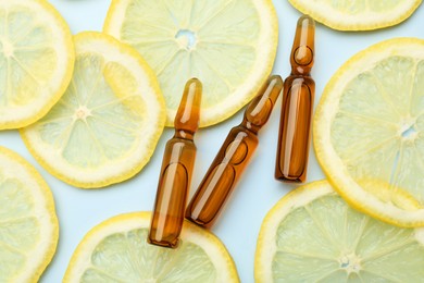 Skincare ampoules with vitamin C and slices of lemon on light blue background, flat lay