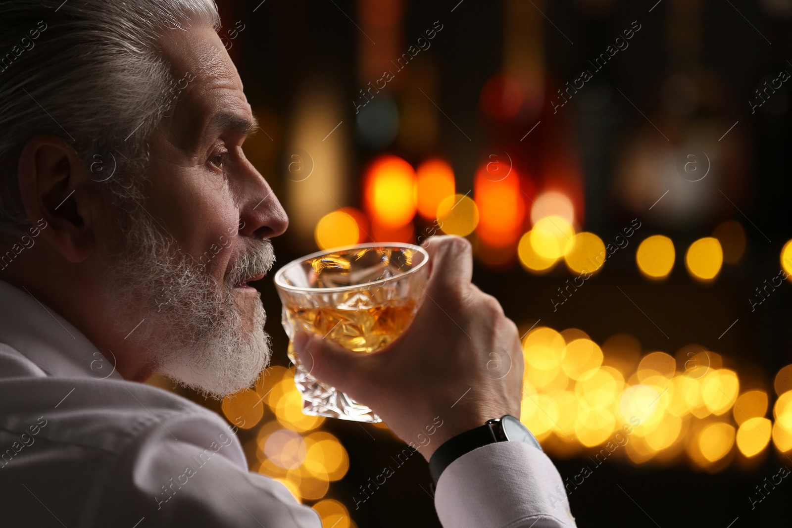 Photo of Senior man drinking whiskey against blurred lights, closeup