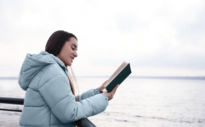 Woman reading book near river on cloudy day