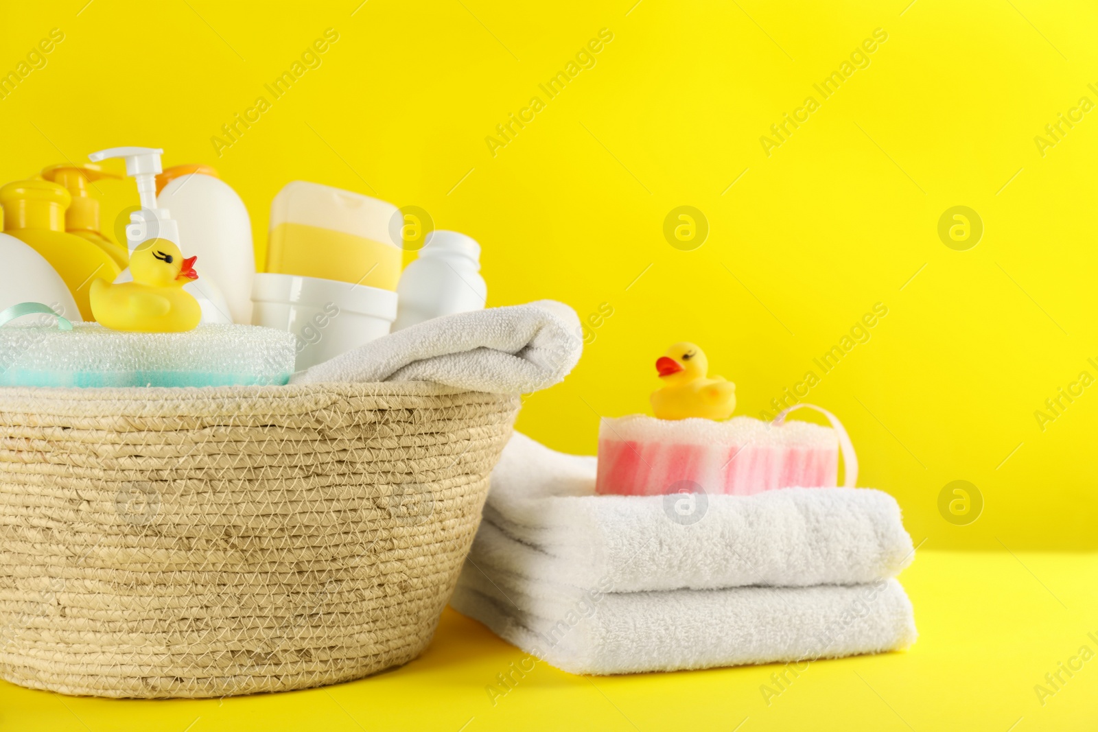 Photo of Basket with baby cosmetic products and accessories on yellow background