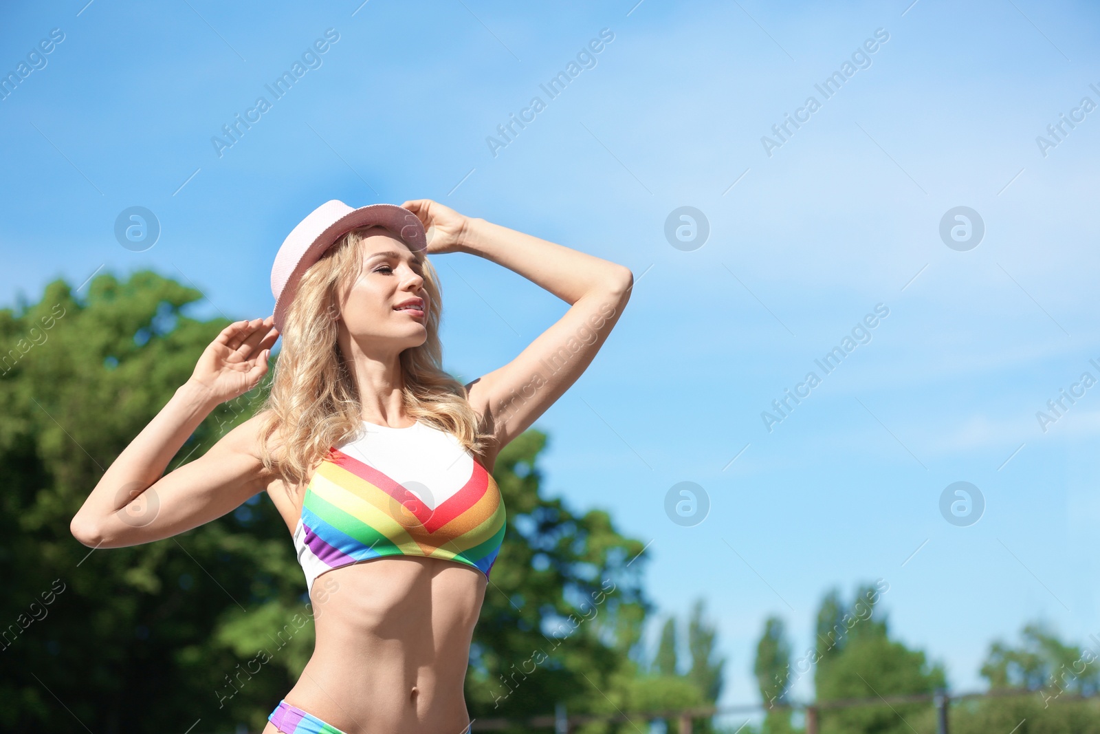 Photo of Sexy young woman in stylish bikini with hat against blue sky on sunny day. Space for text