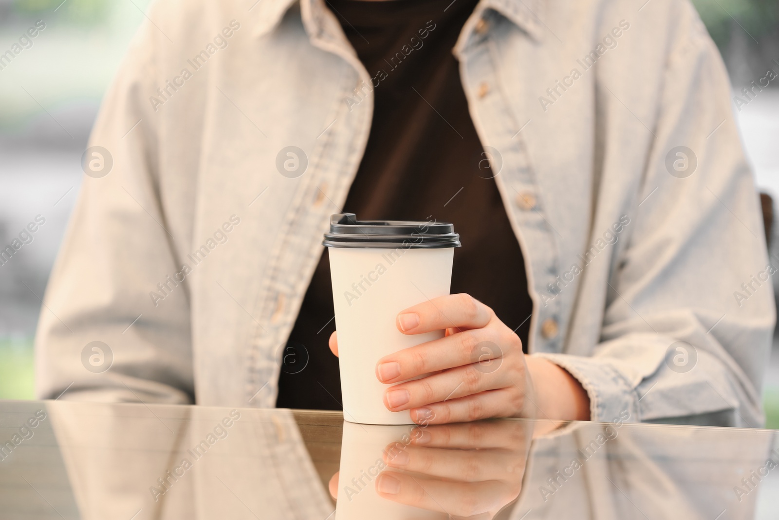 Photo of Woman holding takeaway paper cup at table, closeup. Coffee to go