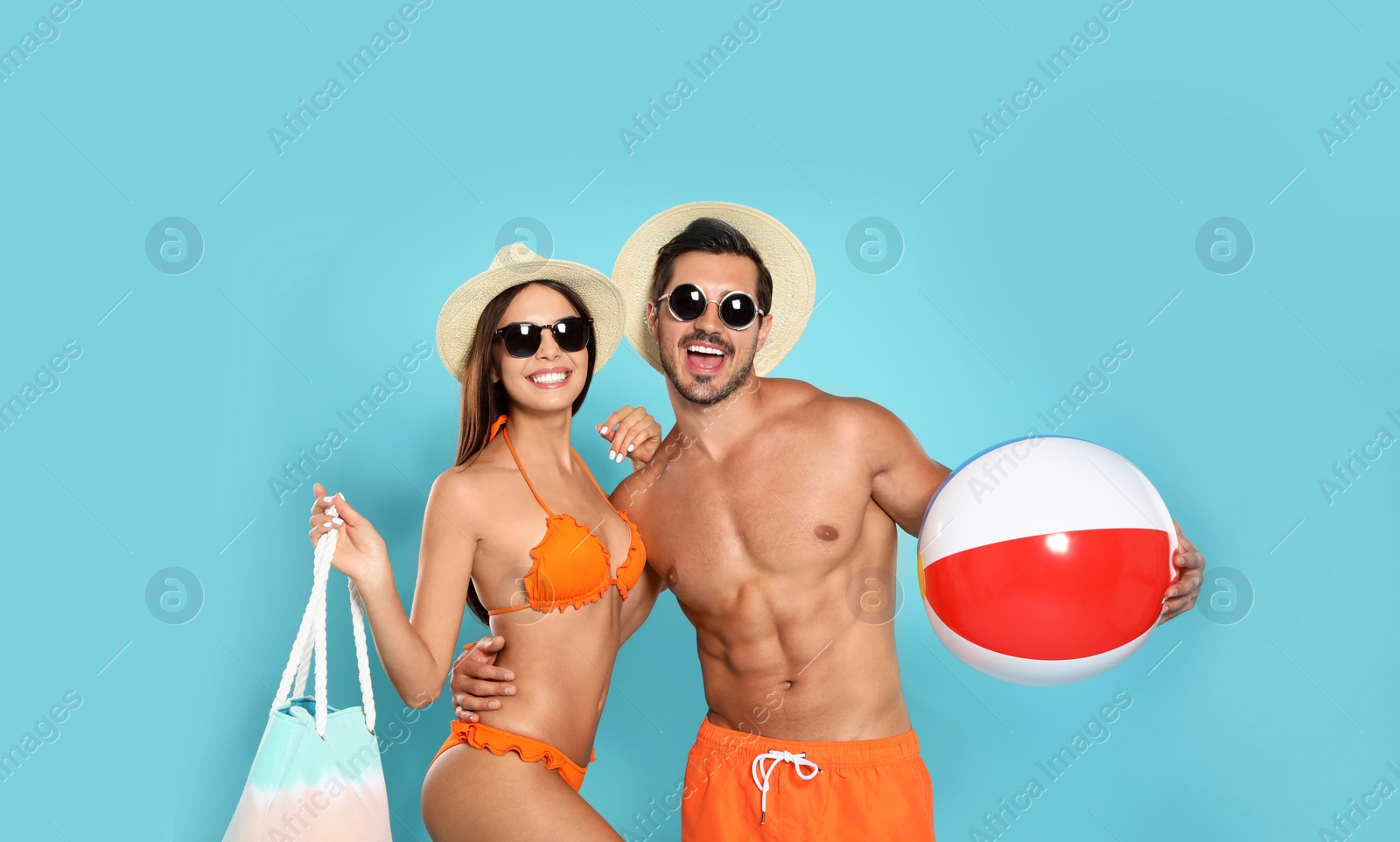 Photo of Young attractive couple in beachwear with ball and bag on blue background