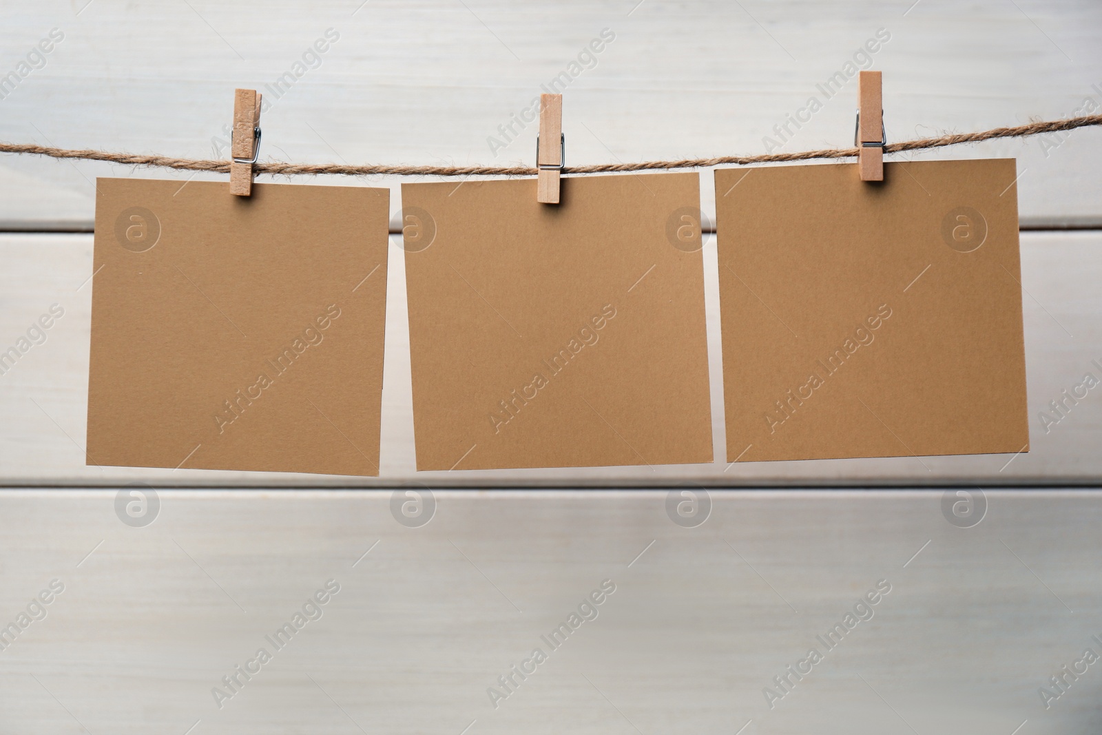 Photo of Clothespins with blank notepapers on twine against white wooden background. Space for text