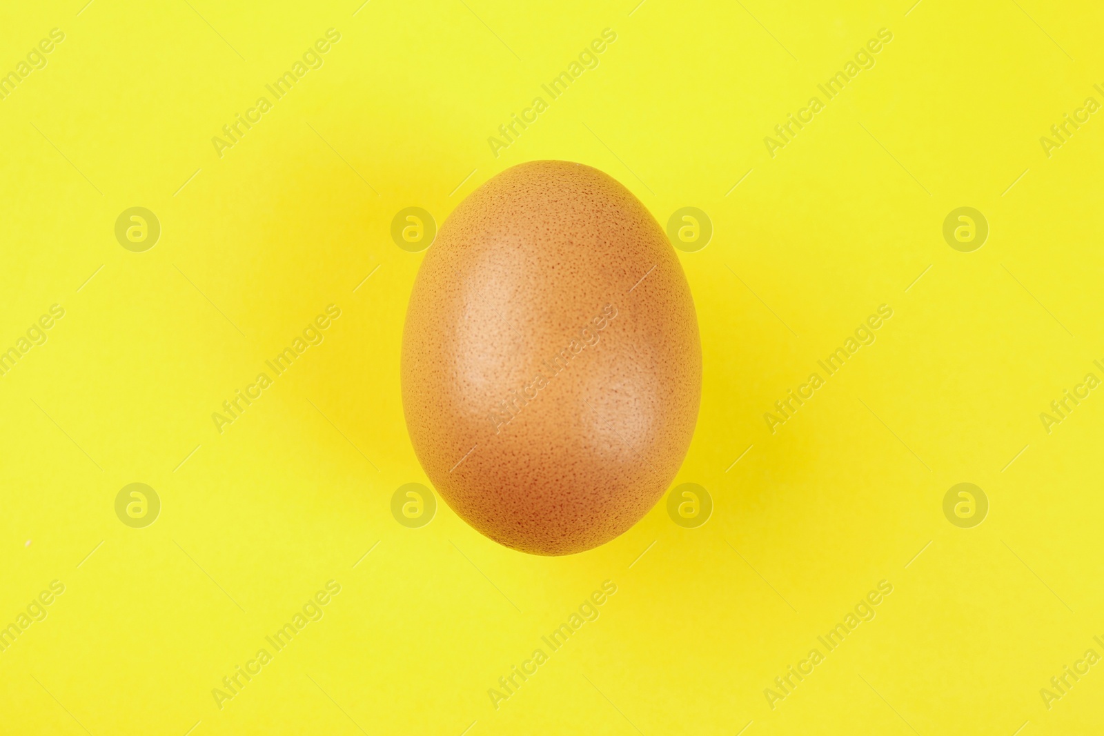 Photo of Raw chicken egg on yellow background, top view