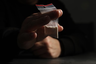 Photo of Drug addiction. Man with plastic bag of cocaine at dark table,selective focus