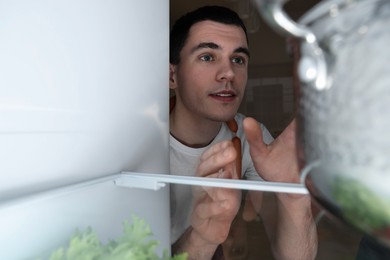 Man near refrigerator in kitchen at night, view from inside