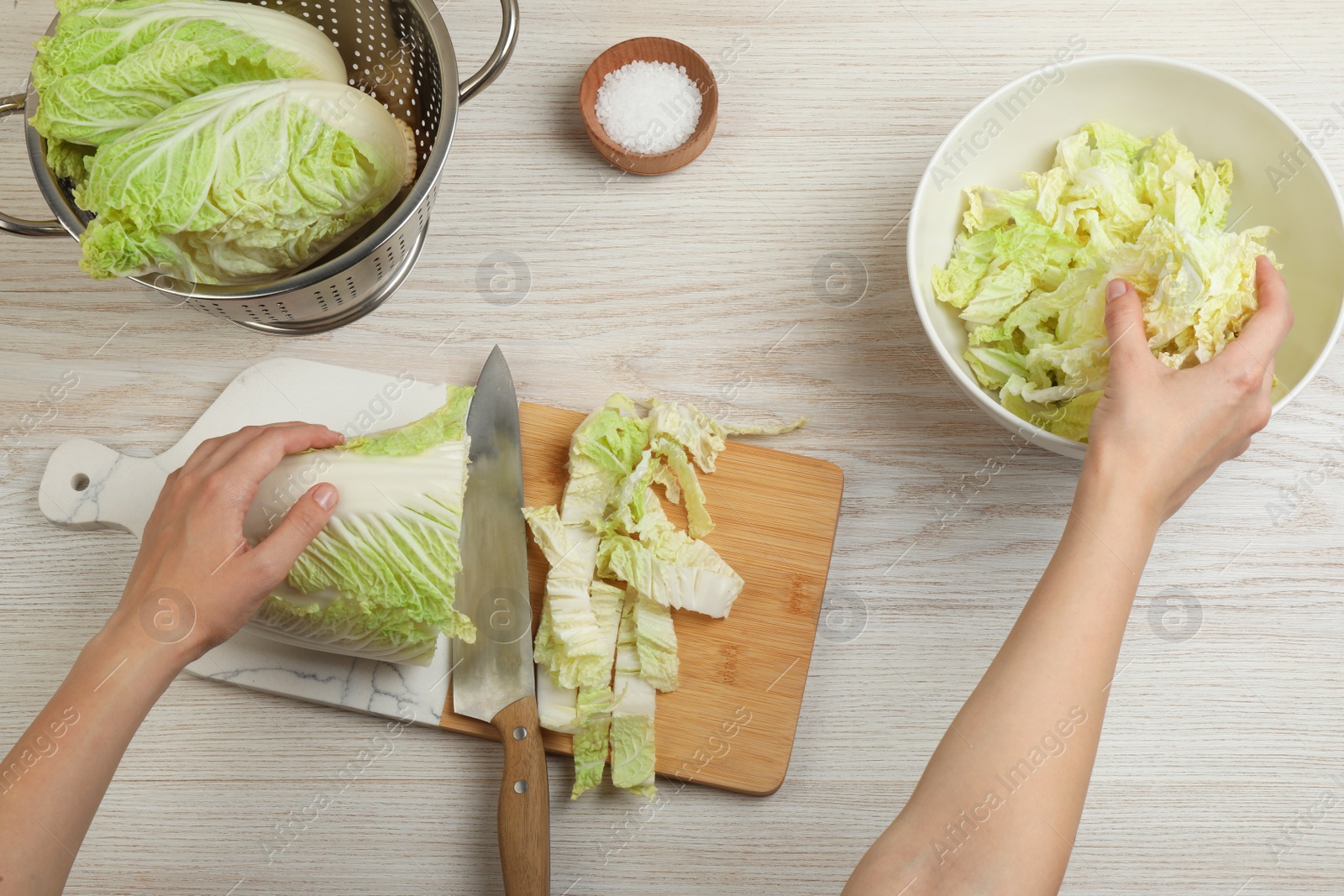 Photo of Woman putting cut Chinese cabbage into bowl at white wooden kitchen table, top view
