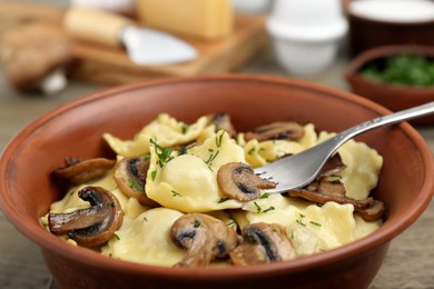 Delicious ravioli with mushrooms and fork served on table, closeup