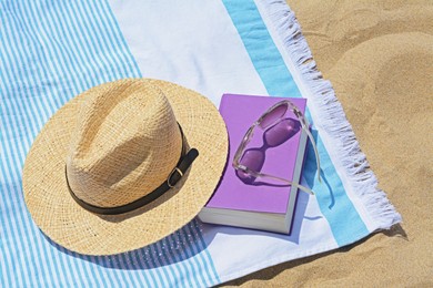 Beach towel with book, straw hat and sunglasses on sand