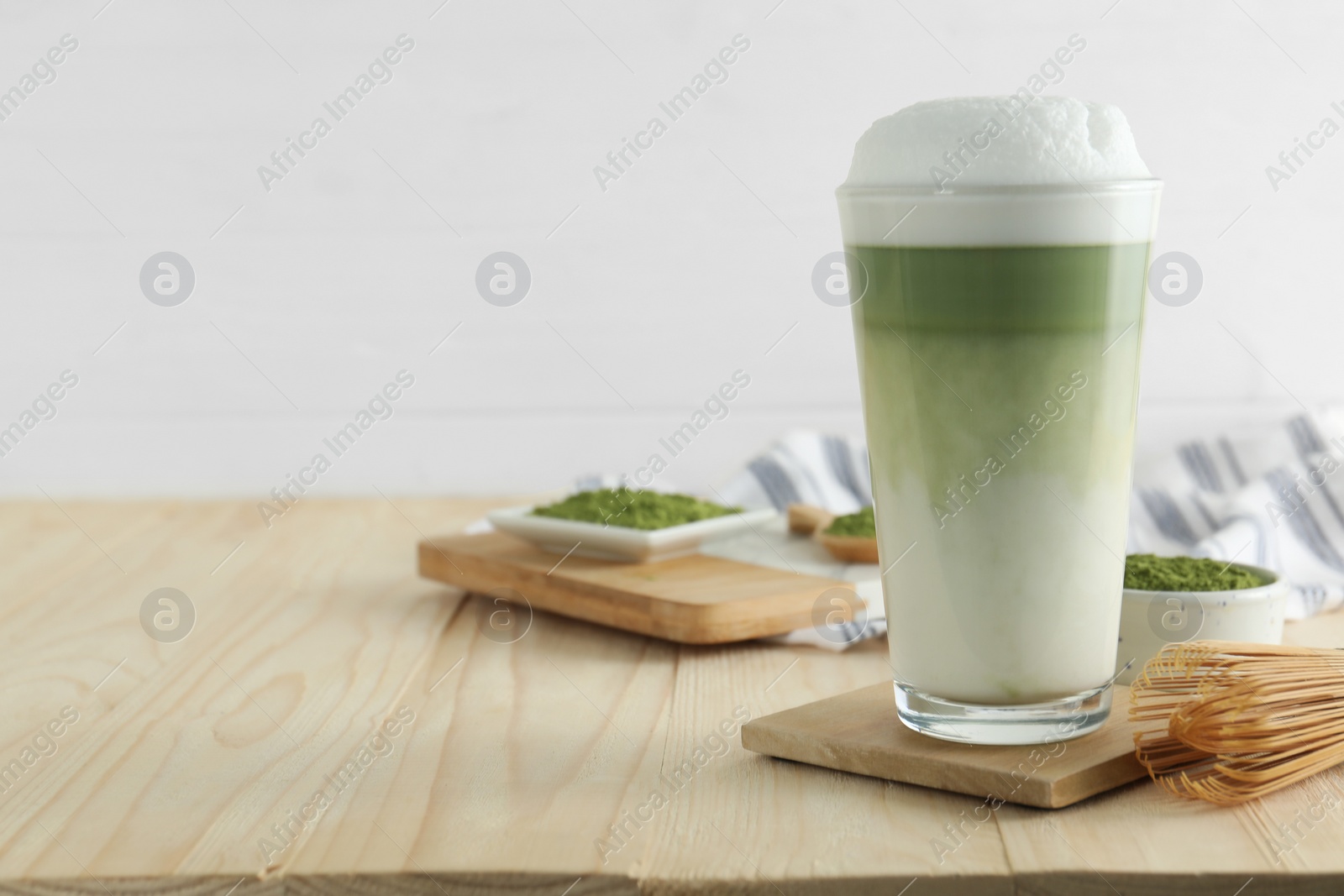 Photo of Glass of tasty matcha latte and bamboo whisk on wooden table. Space for text