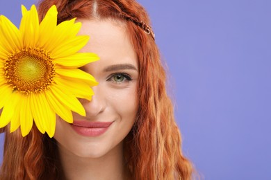 Photo of Beautiful young hippie woman covering eye with sunflower on violet background, closeup. Space for text