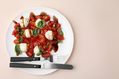Tasty salad Caprese with tomatoes, mozzarella balls, basil and cutlery on beige background, top view. Space for text
