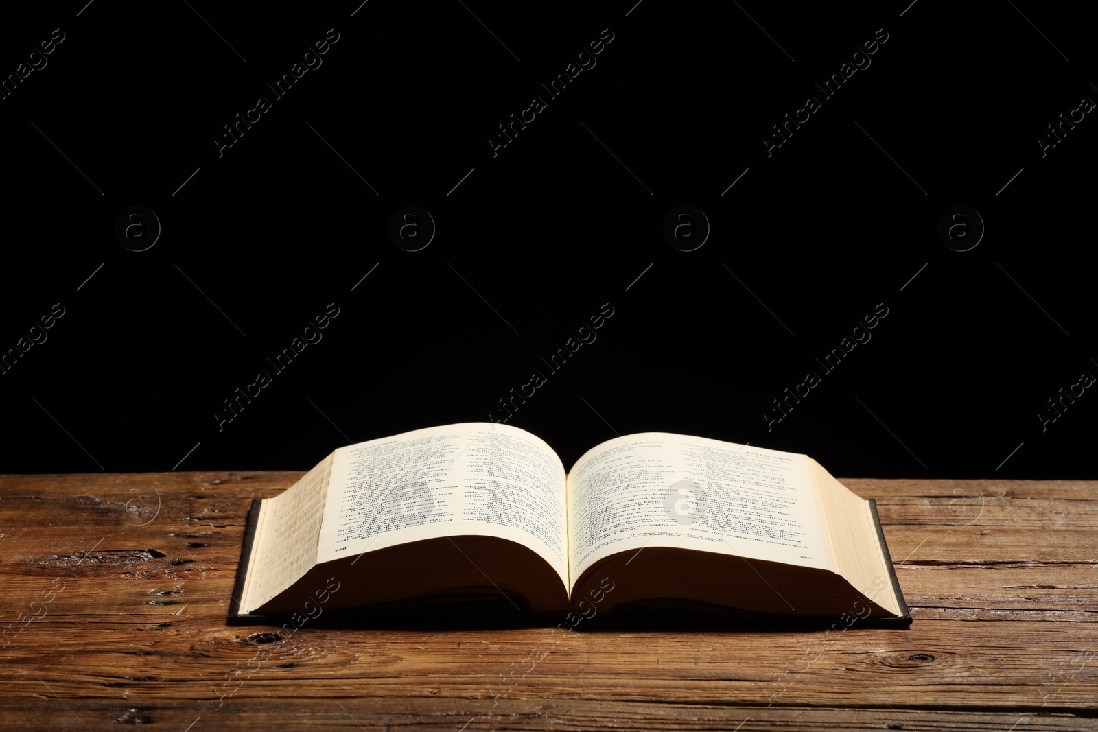 Photo of Bible on wooden table against black background, space for text. Religion of Christianity